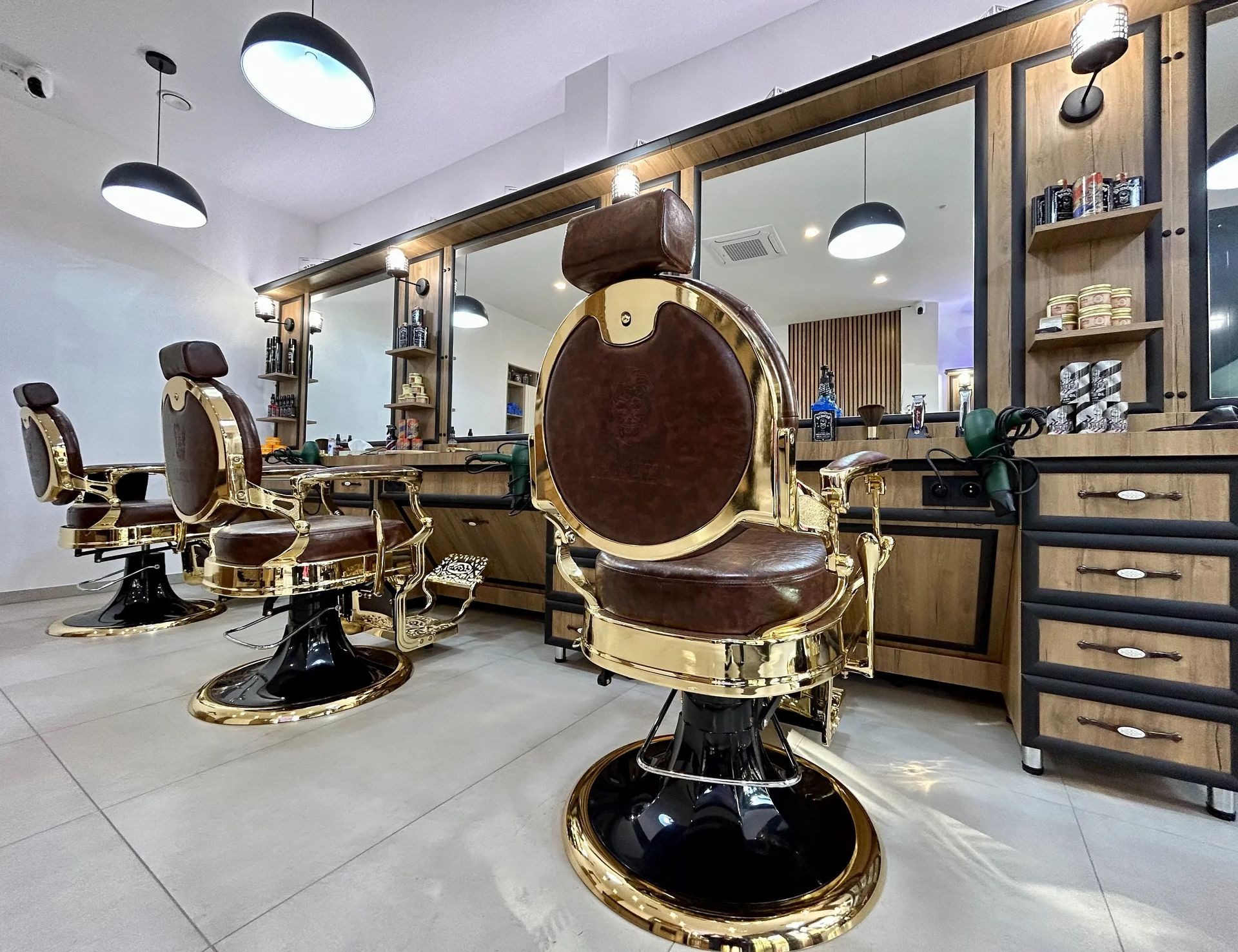 Barber shop interior with vintage brown leather and gold chairs in front of mirrors and shelves.