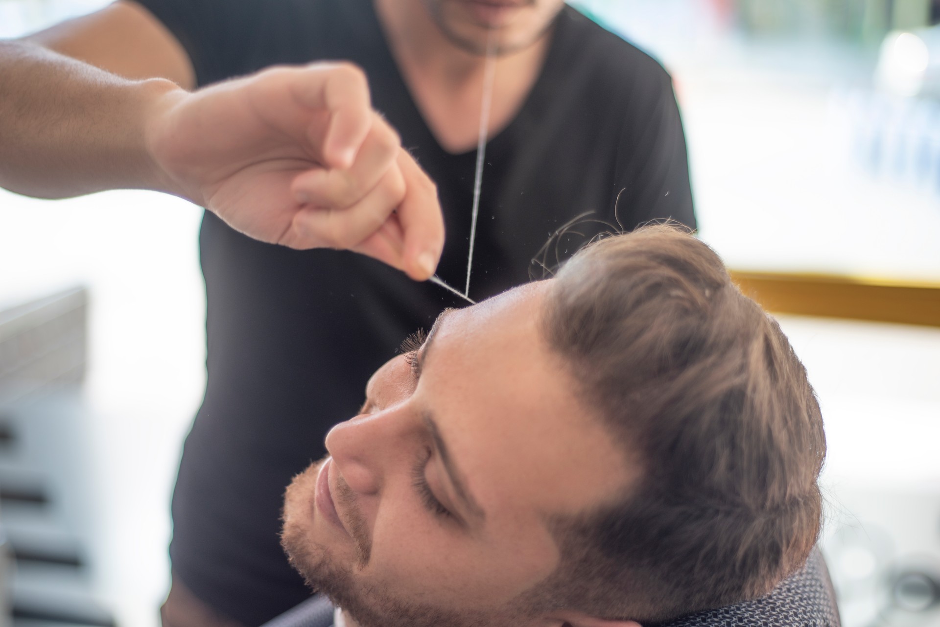 Tiré du barbier remodelant les sourcils du jeune homme dans le salon de coiffure